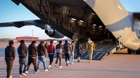 US Government A queue of men with chains around their waists walk into a US military plane