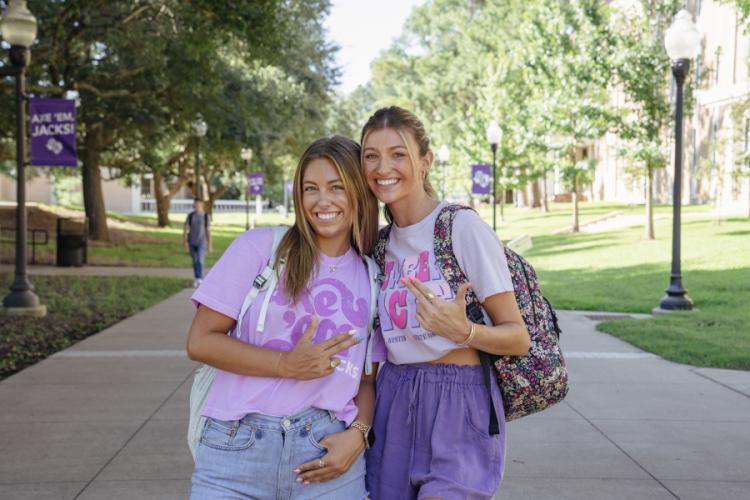 Two students showing the axe 'em hand sign stand together on the SFA campus